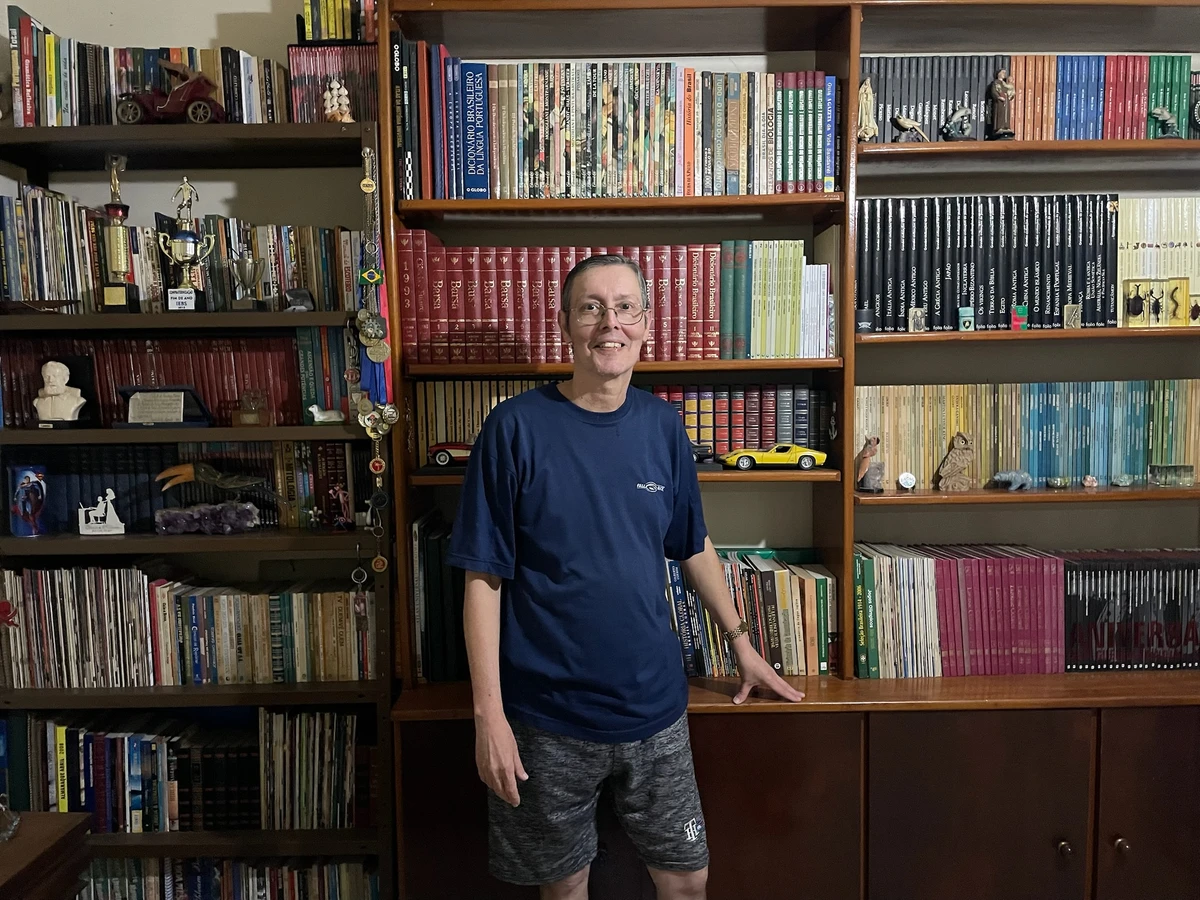 Jornalista Roberto Rodrigues posa para foto em frente à estante com sua coleção de livros.