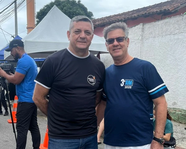 Dois homens adultos em pé sorrindo um ao lado do outro.