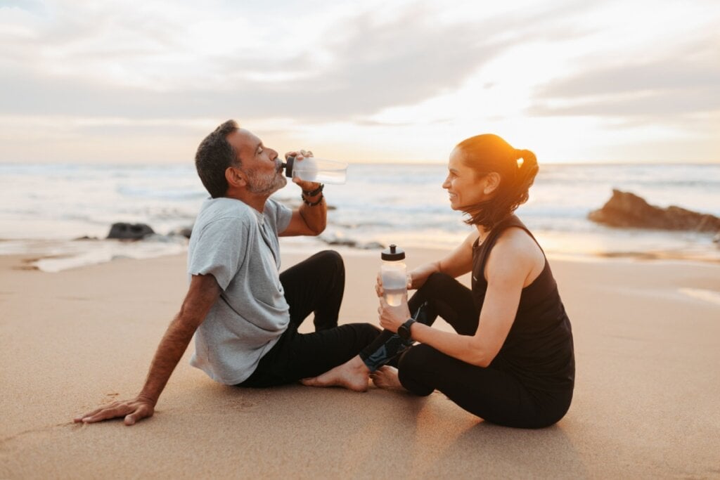 A perda de líquidos é muito maior na praia; por isso, beber água antes, durante e depois do treino é fundamental (Imagem: Prostock-studio | Shutterstock)