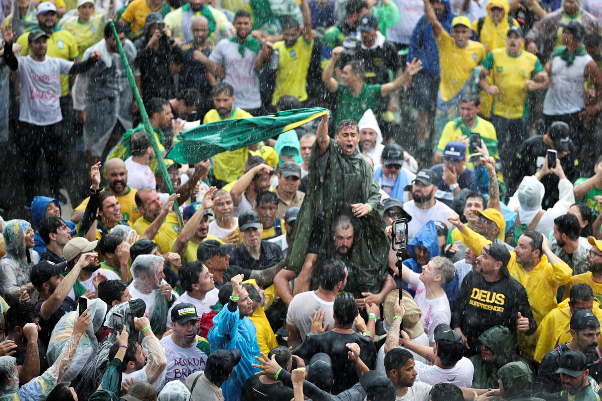 Opposition congressman Nikolas Ferreira sits on a man's back while waving a Brazilian flag, during a march entitled 
